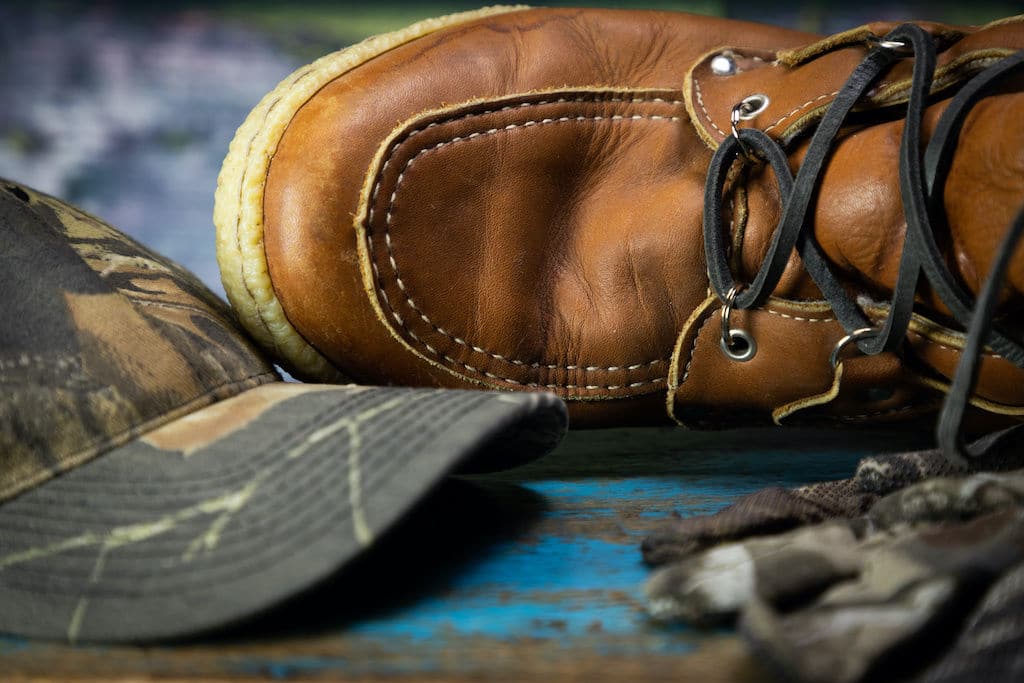 A leather upland hunting boot lying next to a camo hat
