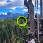 Compound bow with a three-pin sight aiming an arrow towards the mountains