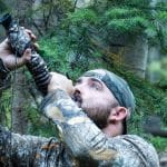 Hunter dressed in camo blowing into an elk bugle call in a forest