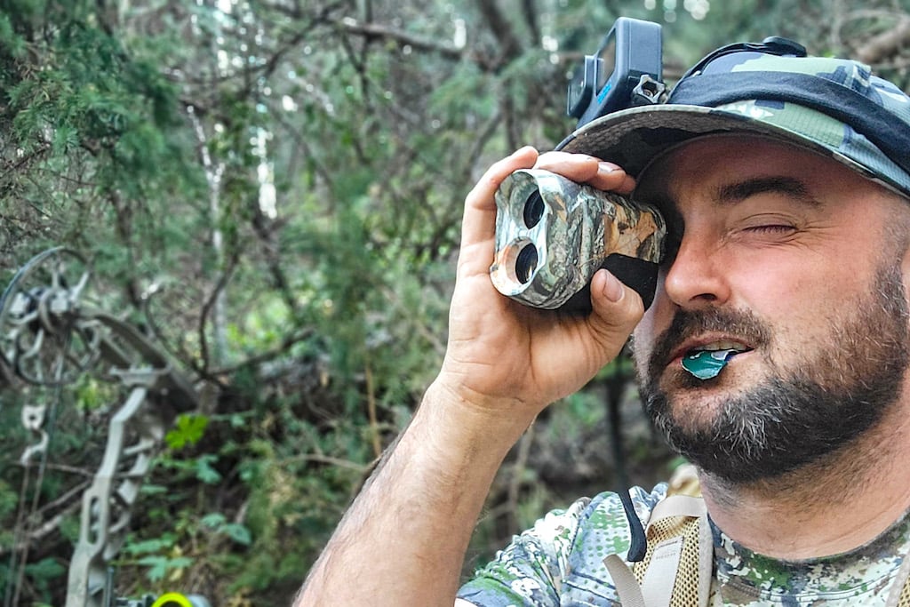 Hunter dressed in camo looking through a laser rangefinder on a 2022 archery elk hunt