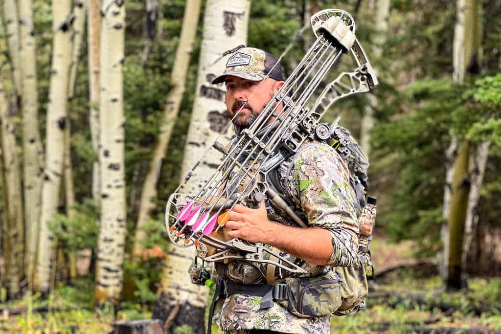 Elk hunter with his compound bow over his shoulder looking into the woods