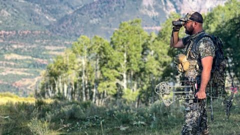 Hunter dressed in camo looking through binoculars with all of his elk hunting gear on his back