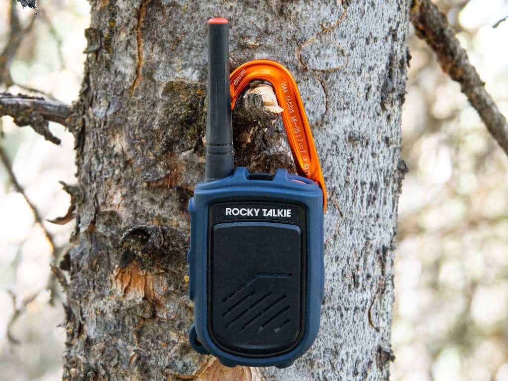 Blue backcountry communication gadget for hiking, hunting, skiing, climbing, and backpacking hanging on a tree branch