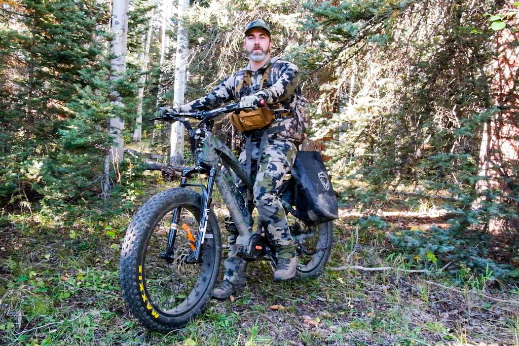 Bearded hunter dressed in camo mountain an electric bike for hunting