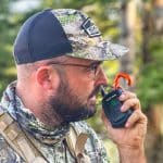 Hunter wearing camo talking into a compact, rugged two-way radio