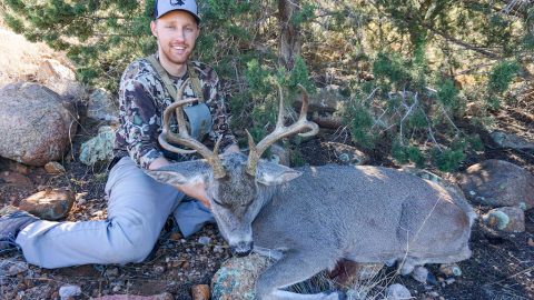 Man wearing a shed hunting hat holding a recently killed coues deer buck