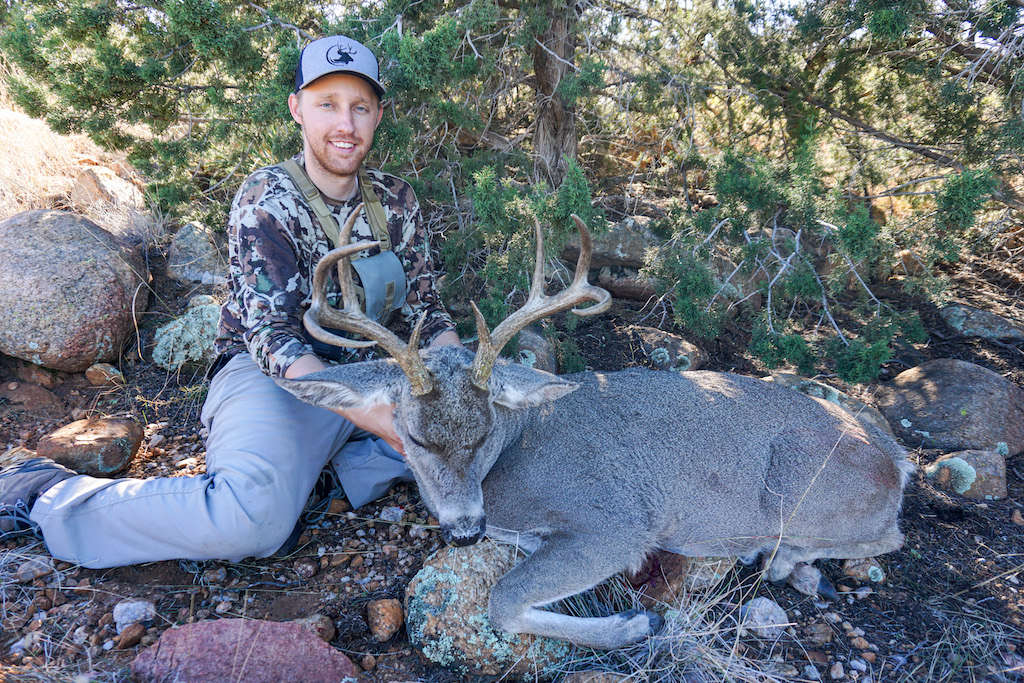 Man wearing a shed hunting hat holding a recently killed coues deer buck