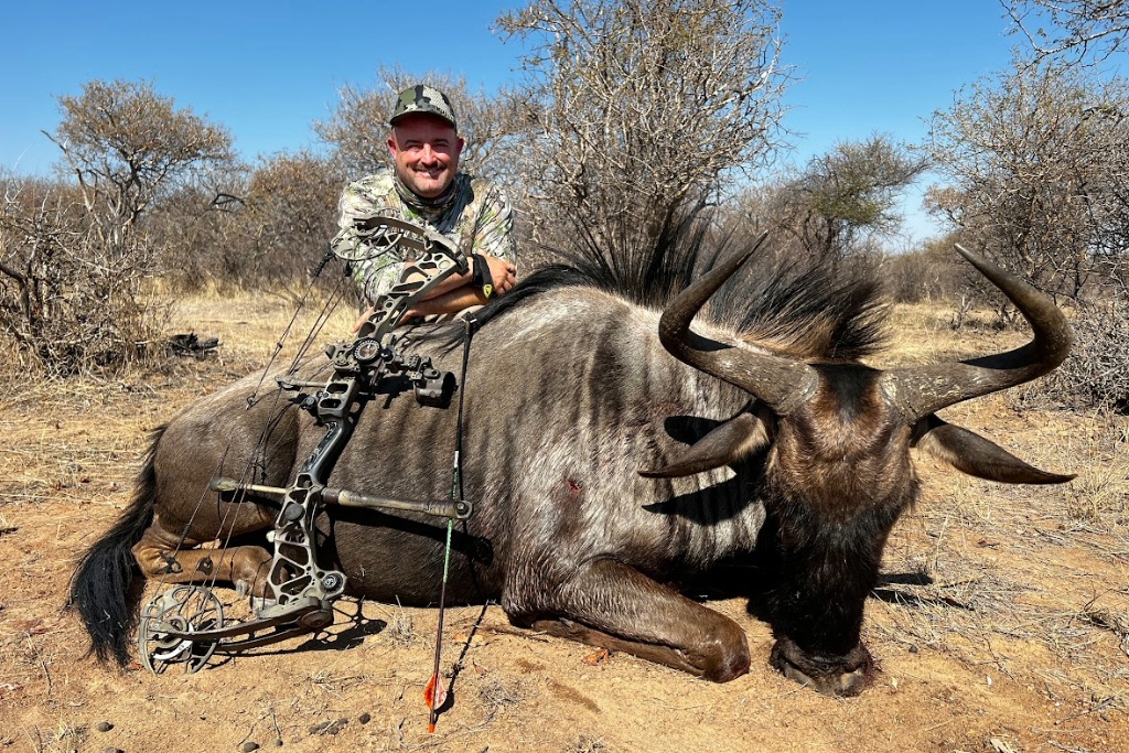 Josh Riley stands over a recently harvested blue wildebeest with a mathews bow and arrow resting against it.