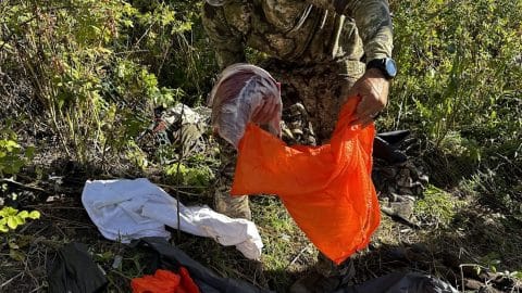 an orange game bag is loaded with a piece of met from an elk by a hunter with a hunting watch on