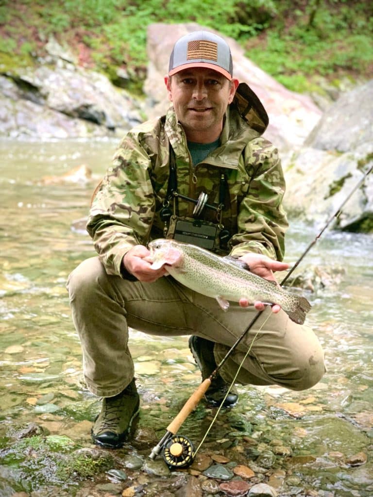 man in river wearing zamberlan boots holding a rainbow trout and standing in a river