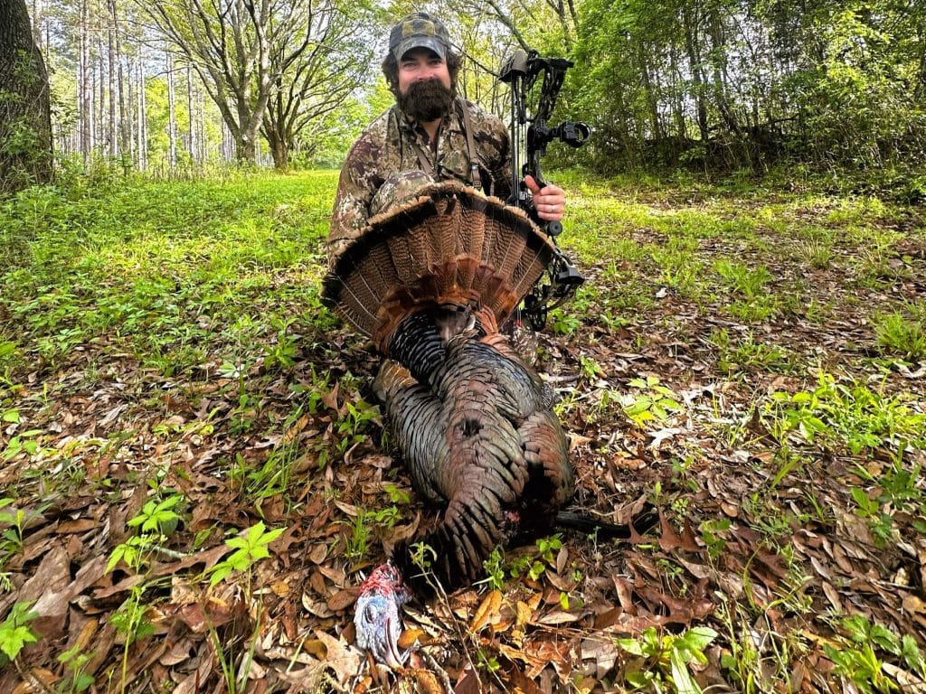 Man holding a compound bow and recently harvested wild turkey