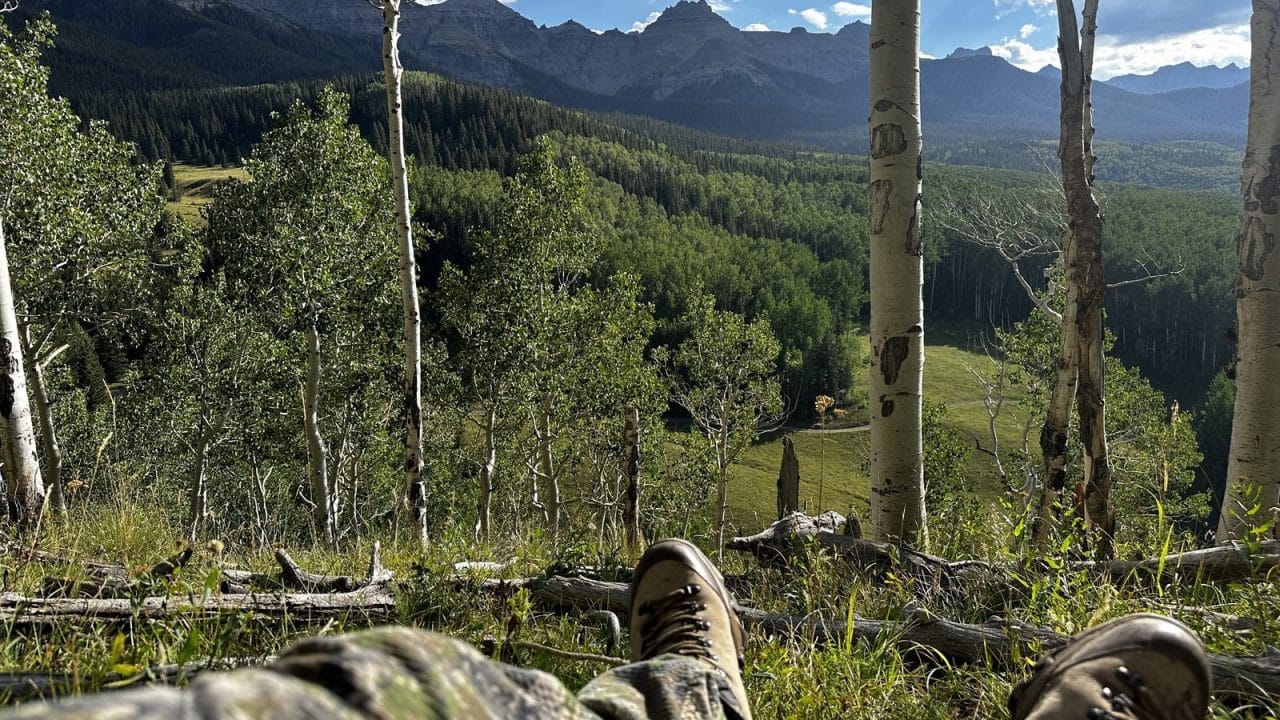 Bowhunter resting with boots up glassing the San Juan Mountains through an aspen stand during Colorado archery elk season