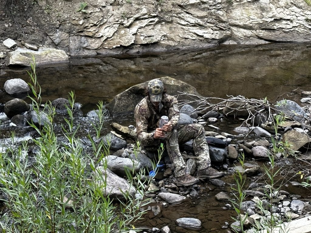 Filtering water at a backcountry creek in Kryptek Obskura Transitional hunting apparel