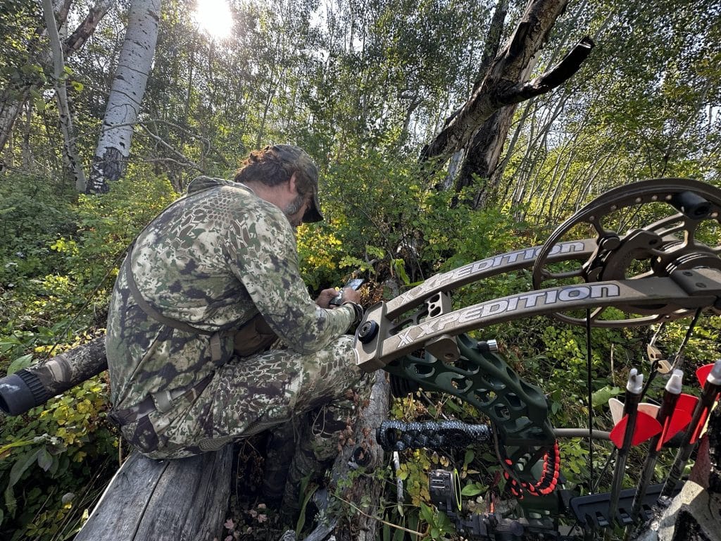 Hunter in a full Kryptek Obskura Transitional jacket and pants glassing from a downed log with a bow