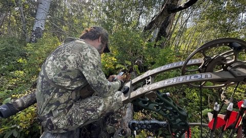 Kryptek Obskura Transitional jacket and pants in the field Hunter in a full Kryptek Obskura Transitional jacket and pants glassing from a downed log with a bow