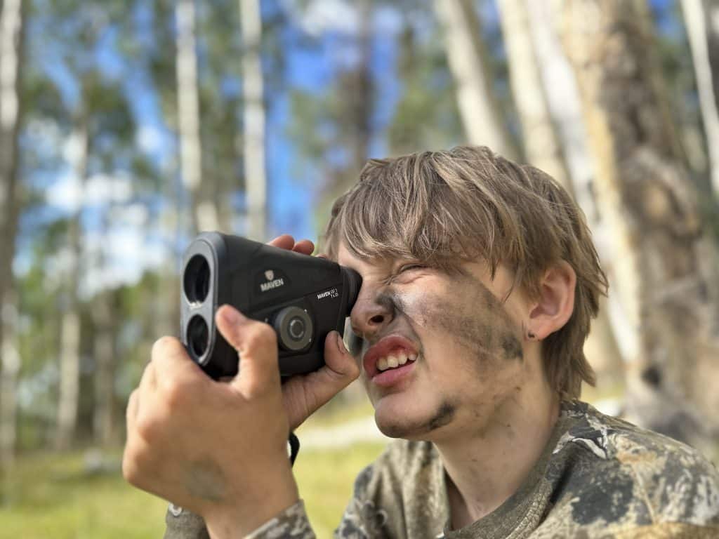 Young bowhunter in face paint ranging distance with a Maven RF.1 rangefinder in a Colorado aspen stand during elk season