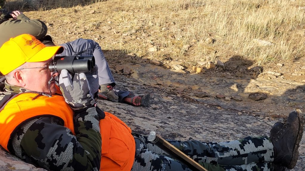 Hunter in blaze orange glassing with Leica Geovid rangefinding binoculars during rifle season